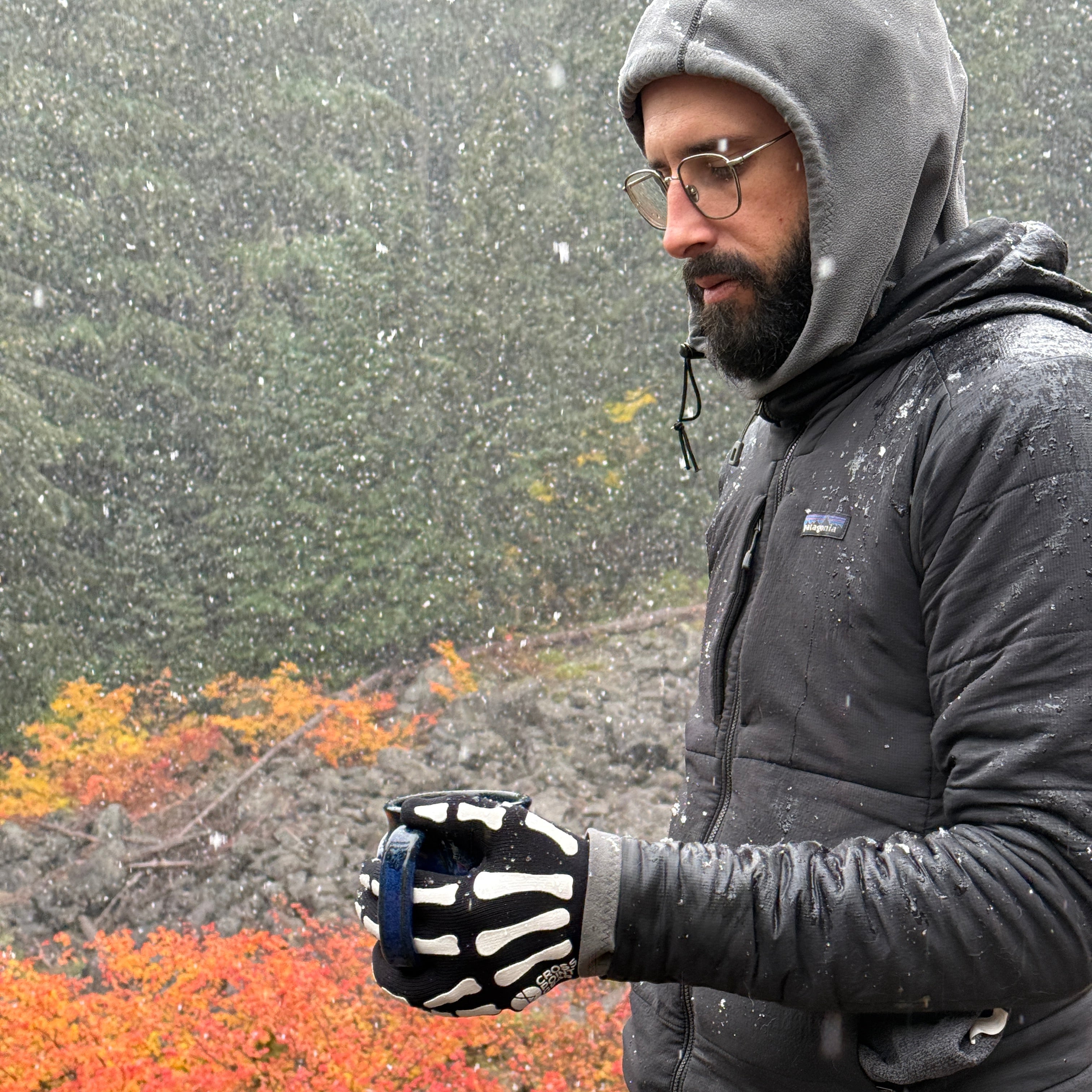 Person wearing a gray hoodie and black gloves with skeleton patterns, standing on a road with autumn foliage.