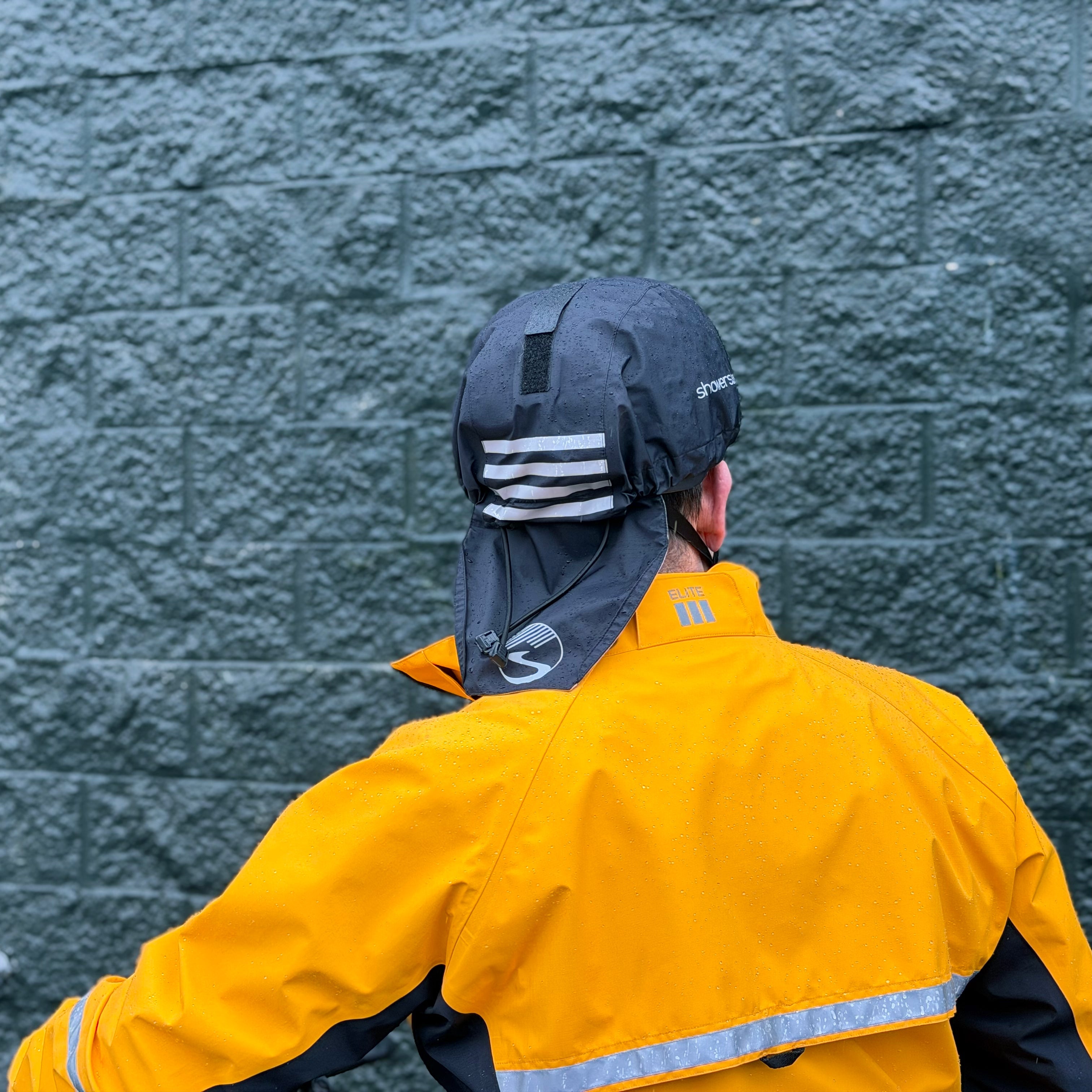 Person wearing a yellow raincoat and black helmet cover against a textured gray wall