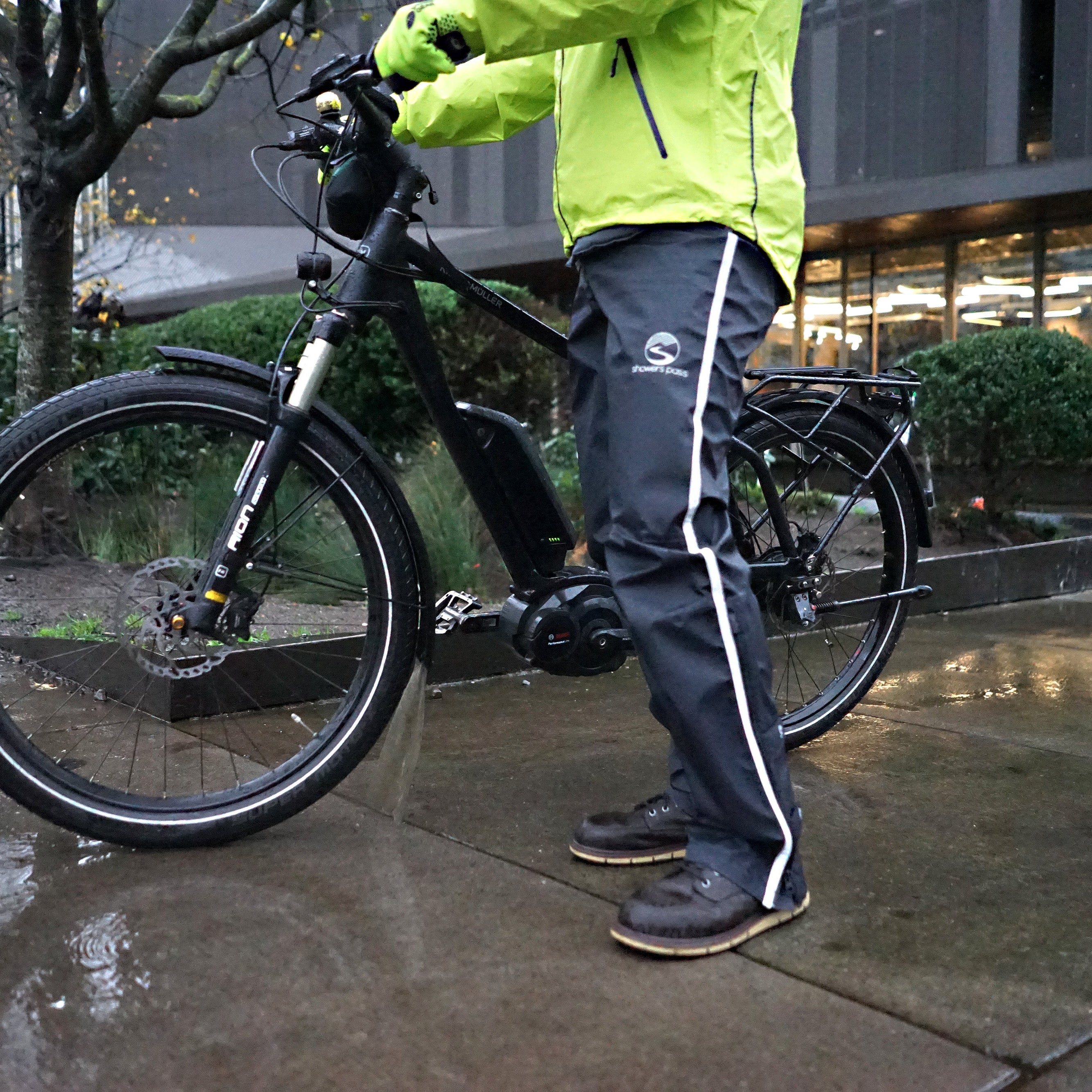 Person in a green raincoat standing next to an electric bike on a wet sidewalk.