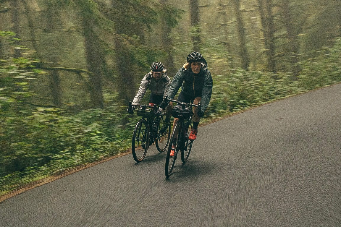 An action shot of a man and woman riding their road bikes around a corner in the rain