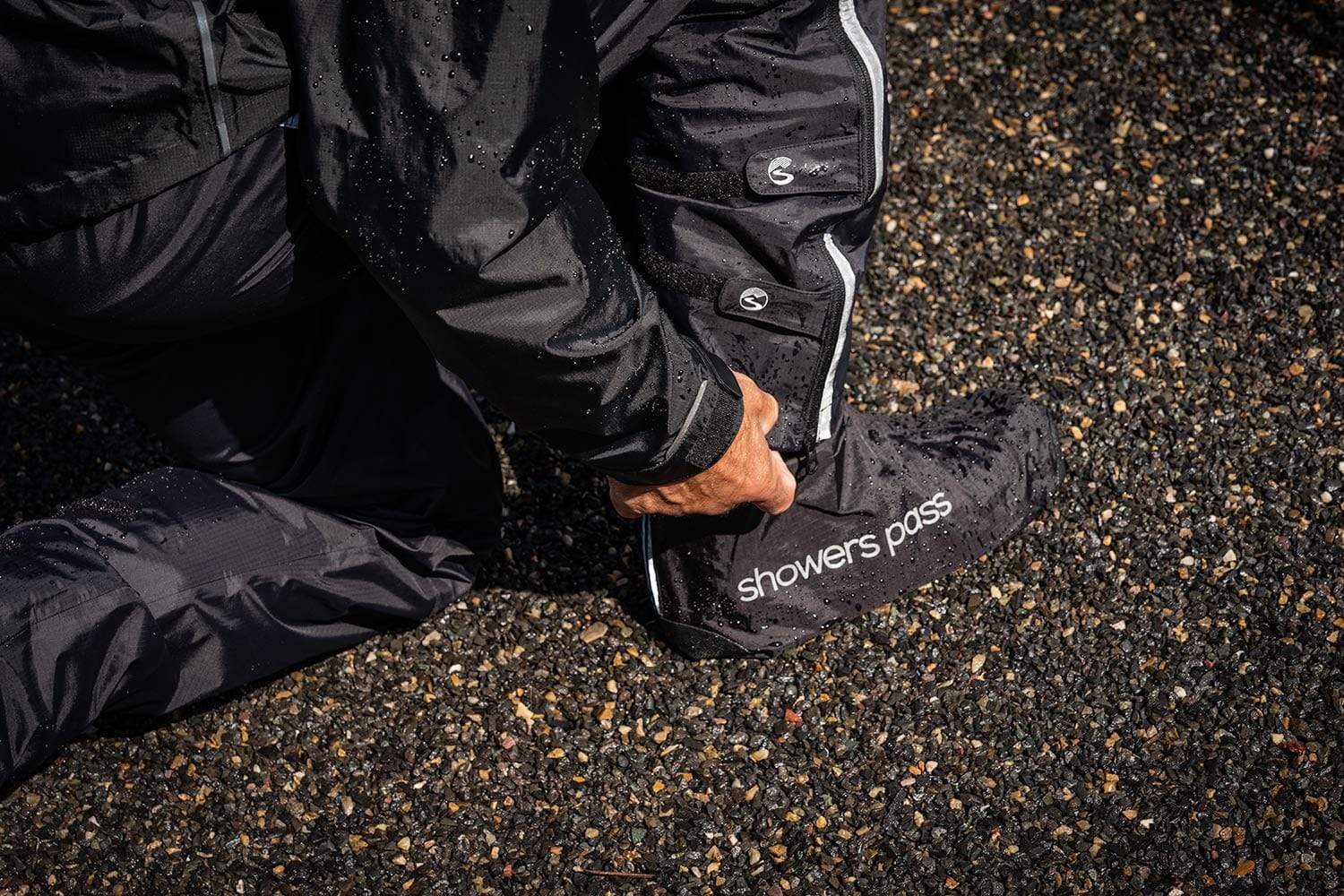 A close up shot of a man adjusting his rain pants over his waterproof shoe coverings with the brand Showers Pass on it