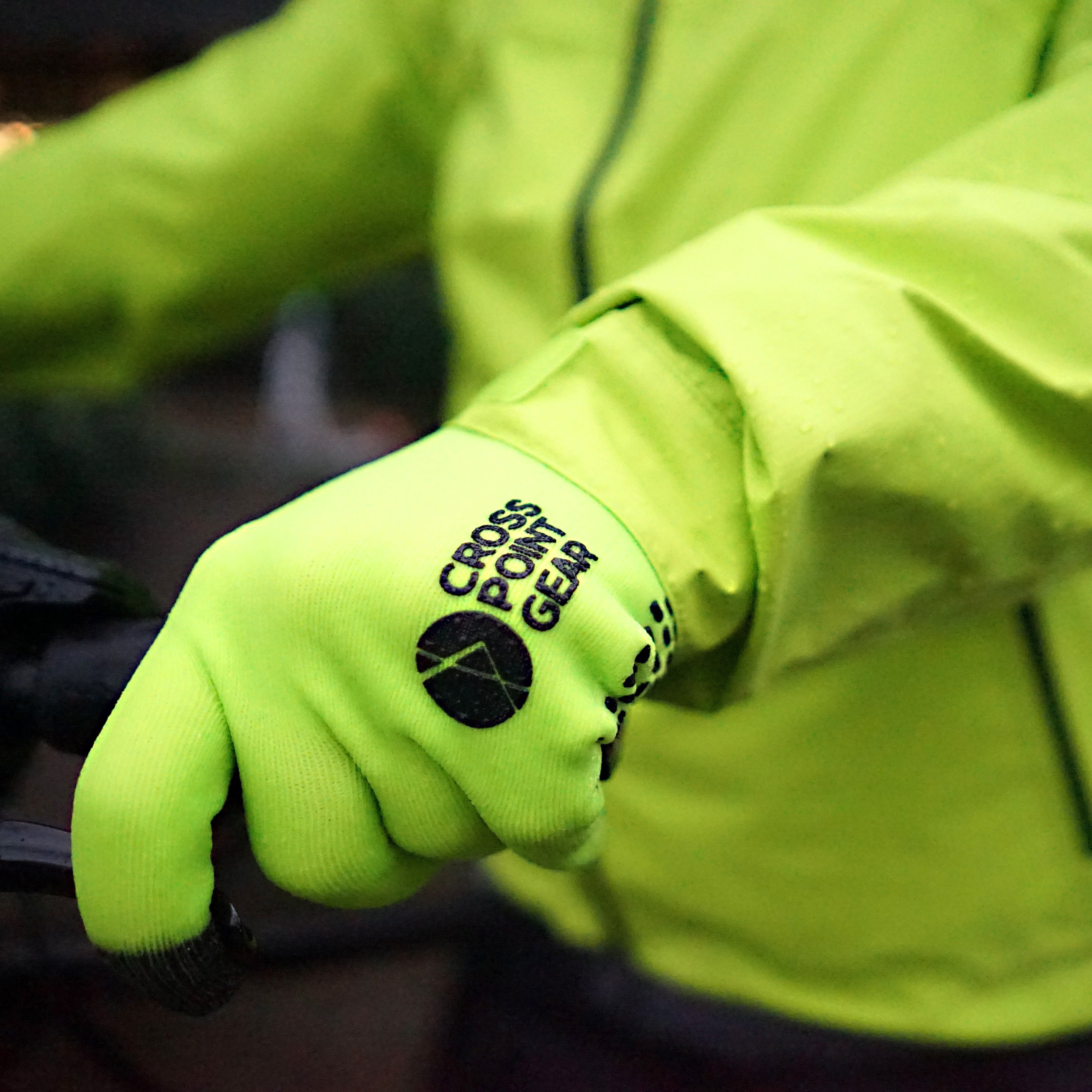 Person wearing a bright green Showers Pass jacket and matching Cross Point Gear gloves.