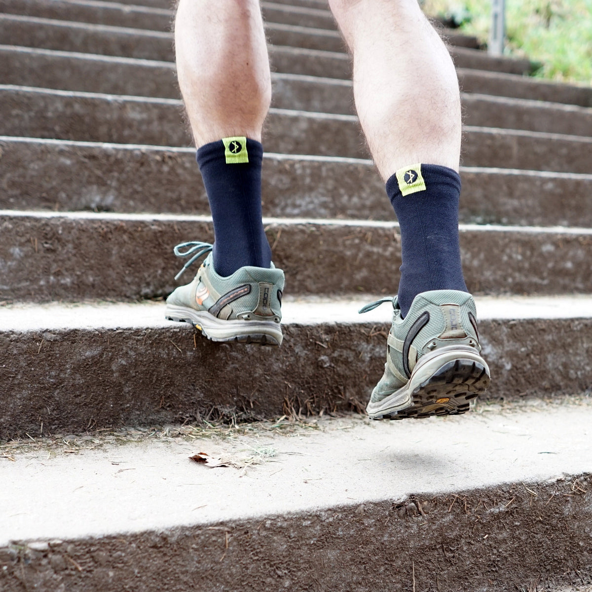 A person climbs stairs wearing sneakers and Cross Point Gear superlight waterproof socks with visible logos.