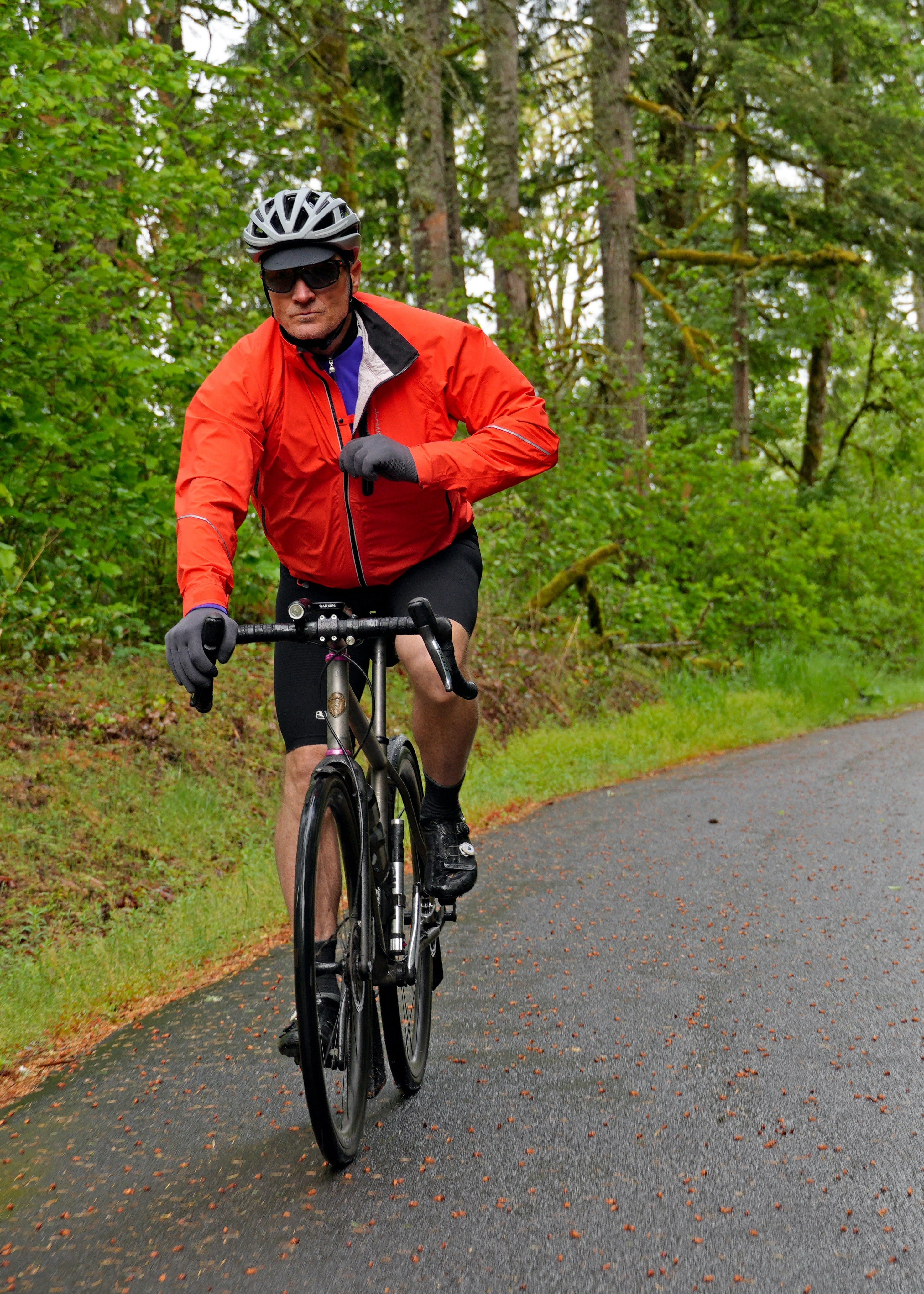Two cyclists wearing Showers Pass jackets on a wet winding road surrounded by trees